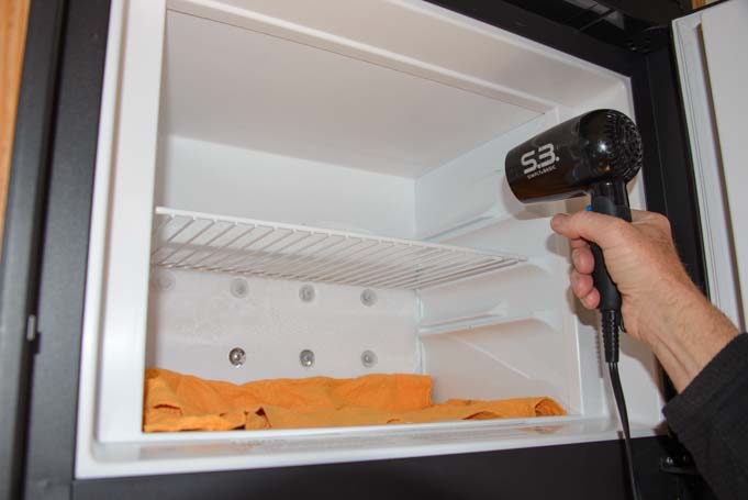 Defrosting RV refrigerator hair dryer on freezer with towels