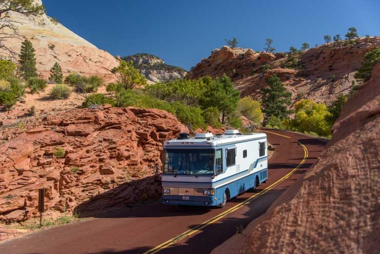 RV motorhome drives through red rock scenery near Coral Pink Sand Dunes State Park in Utah