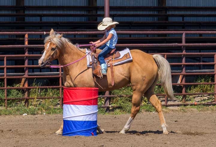 Young barrel racer rounds the barrel on her horse-min