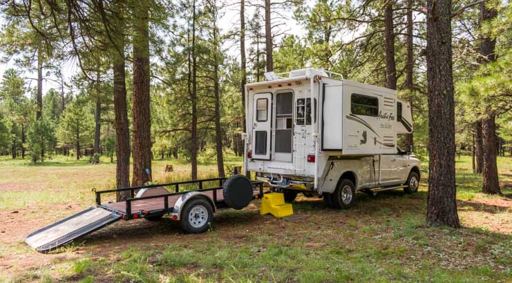 Campsite with Arctic Fox 860 truck camper, dually truck, RZR and flat bed trailer
